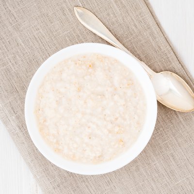 Large bowl of tasty and healthy oatmeal for Breakfast, morning meal. Top view, close up, white wooden rustic table.