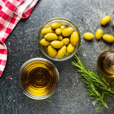 Green olives and olive oil in glass bowl.