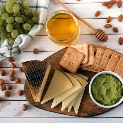 Cheese served with grapes, guacamole, honey, crackers and nuts on a light wooden background. Top view