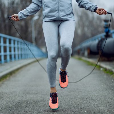 Unrecognizable sportswoman jumping rope on a bridge.