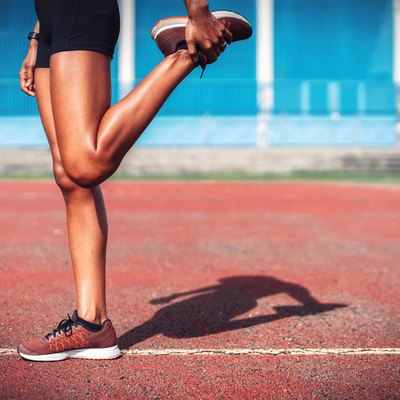 Low Section Of Female Athlete Stretching Leg On Sports Track