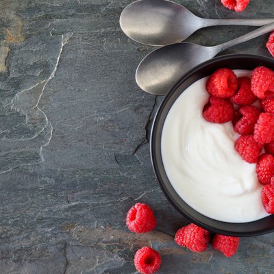 Greek yogurt with raspberries, top view, side border on a slate background