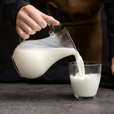 Woman pouring fresh milk from jug into glass on table