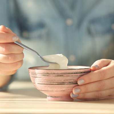 closeup of bowl with yogurt and spoon in female hands