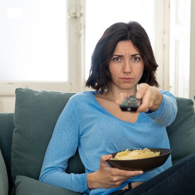 Young upset woman on sofa using control remote zapping bored of bad TV shows and programing . Looking disinterested, aloof and sleepless. People, too much bad television and Sedentary lifestyle.