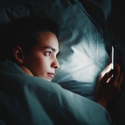 Close-Up Of Woman Using Phone While Lying On Bed In Darkroom