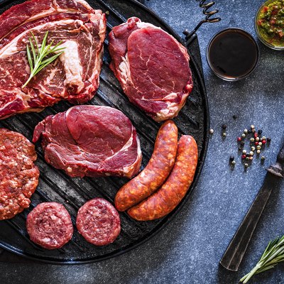 Various cuts of raw meat shot from above on a cast iron grill
