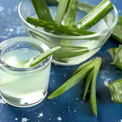 Glassware with fresh aloe vera juice and leaves on color table
