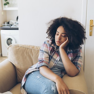 Woman feeling tired after eating sitting on tan chair at home
