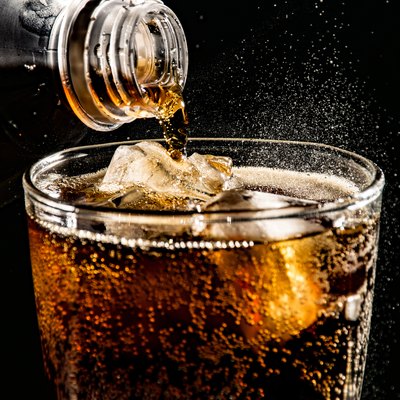 Close-Up Of Drink Pouring In Drinking Glass Against Black Background