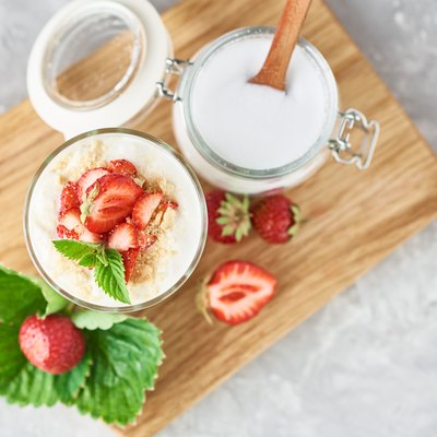 granola or yogurt with strawberry in glass, fresh berries and jar with sugar on a cutting board, top view