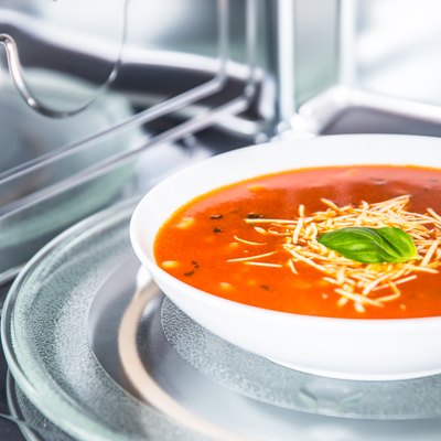 Inside view of new clean staniless microwave oven with a tomato soup in white plate