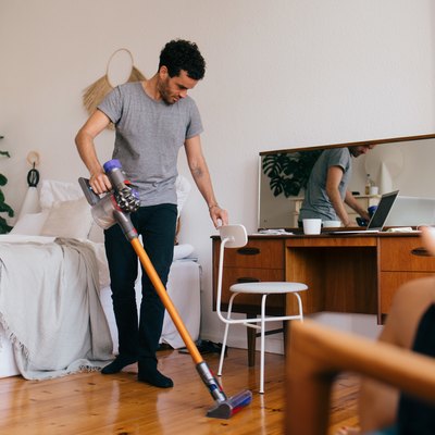 Full length of man cleaning bedroom with vacuum cleaner