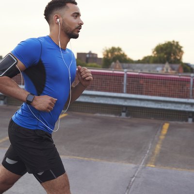 Young male athlete running on a road, side view close up