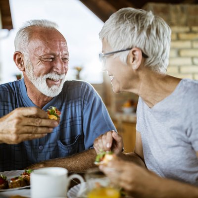 A happy senior couple talking while eating breakfast on a balcony.