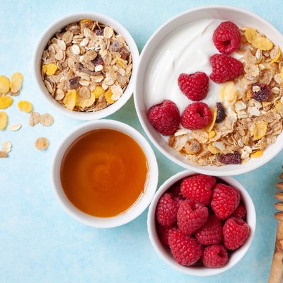 Greek yogurt in bowl with raspberries, honey and muesli on blue table top view.