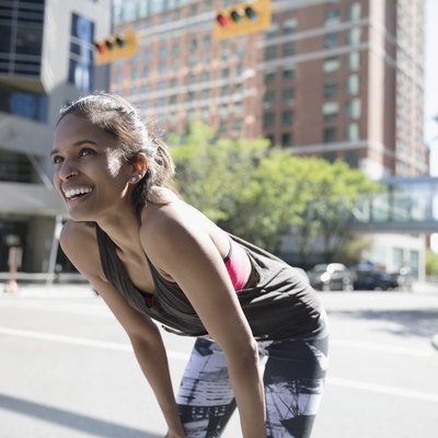 Smiling female runner resting with hands on knees on sunny urban street