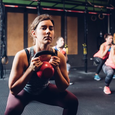 Women training in gym, squatting and lifting kettle bells