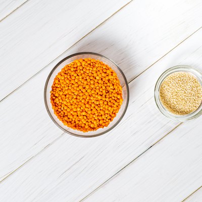 Glass plates with red lentils, sesame seeds and a large glass plate stand on wooden table