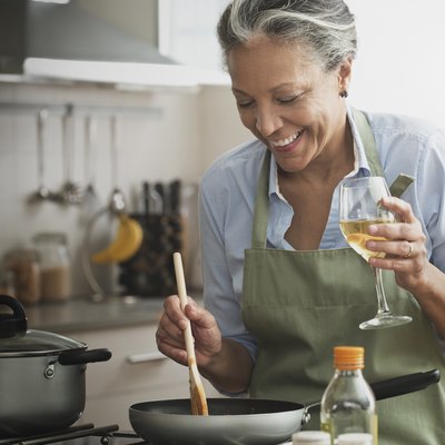 Hispanic woman cooking with wine in kitchen