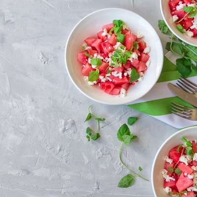 Fresh organic salad with watermelon, feta cheese and mint in bowls on light gray concrete background.