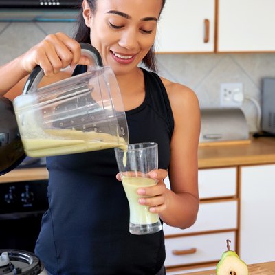 woman pouring green smoothie into glass