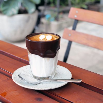 A glass of iced cocoa coffee latte; upper layer is black espresso shot lower is fresh milk decorated with melted black cocoa and marshmallow.