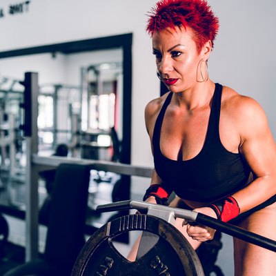 Muscular woman female athlete work out at the gym training using T-bar rowing back workout bodybuilding fitness