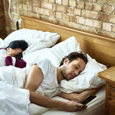 Woman fast asleep next to partner who is checking his smartphone
