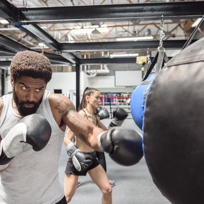 Man and women wearing boxing gloves hitting heavy bags