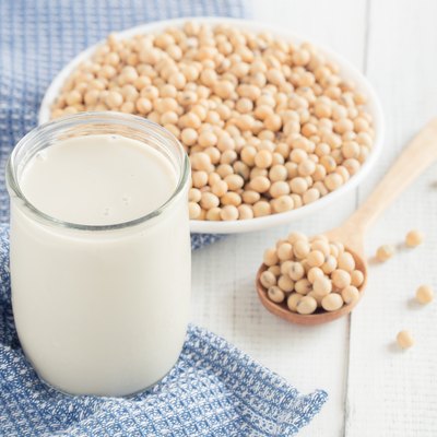 A glass of soy milk on a white wood floor with soybean as a background.