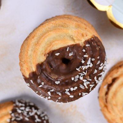 Round ring shaped sweet biscuits with half side glazed with chocolate and topped with coconut sprinkles