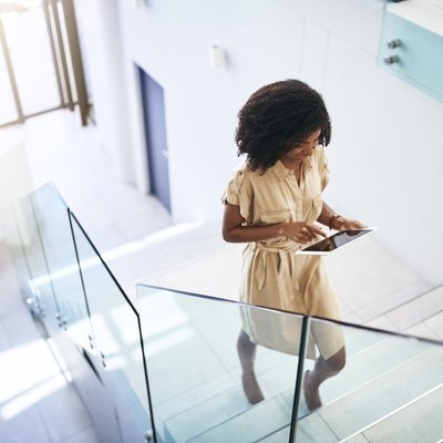 A professional woman walking up the stairs in her office building while working on a tablet
