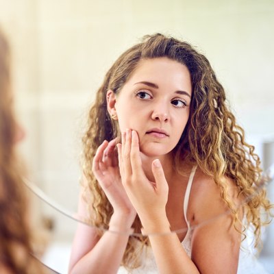 woman looking in mirror touching face