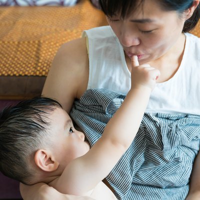Asian mother breastfeeding and hugging her baby.