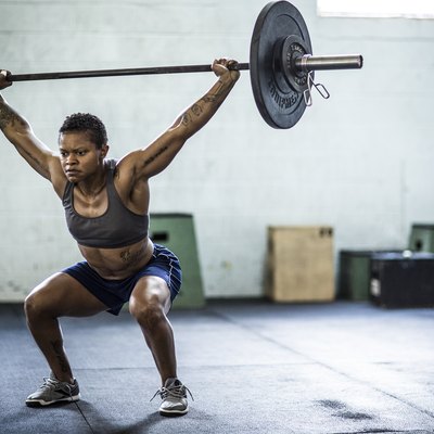 woman doing an overhead barbell squat in the gym as part of a superset workout