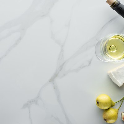 top view of glass of wine, cameembert cheese pieces, figs and pears on white marble tabletop