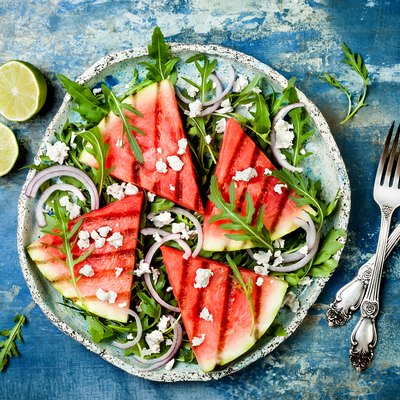 Fresh summer grilled watermelon salad with feta cheese, arugula, onions on blue background