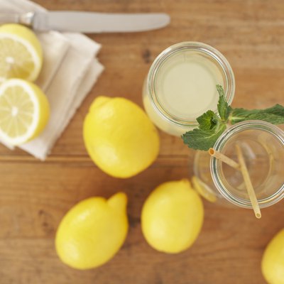 Carafe of lemon juice, sliced and whole lemons on wood, elevated view