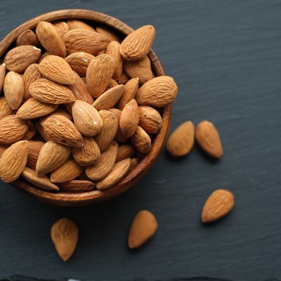Almonds nut close-up.Raw almonds in a round wooden cup on a black slate background. Nuts in a cup.Vegetarian and vegan food.