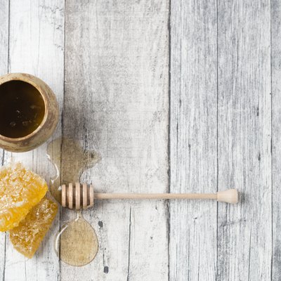 Honeycombs, clay pot and honey dipper on wood