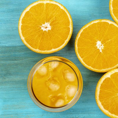 A photo of a glass of fresh orange juice with orange halves, shot from above on a vibrant blue background with a place for text