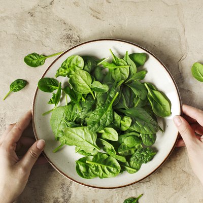 Woman's hands holding a plate with fresh spinach.
