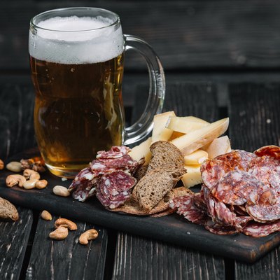Mug of beer and snacks on wooden board on dark wood background. Kielbasa, cheese, nuts, toasts
