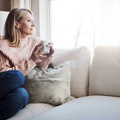 A woman drinking coffee on her couch while looking out the window