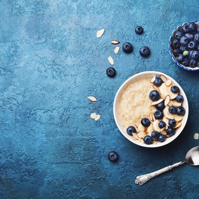 Bowl of oatmeal porridge with banana and blueberry on vintage table top view in flat lay style. Healthy breakfast.