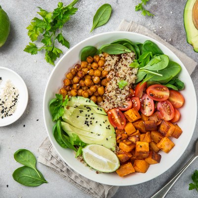 Top view of a bowl of thermic foods, including avocado, quinoa, sweet potato, tomato, spinach and chickpeas