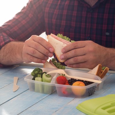 Man is eating healthy food of lunch box sitting at wooden table