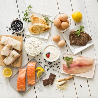Chicken meat, fish, cottage cheese, yogurt and eggs on white table