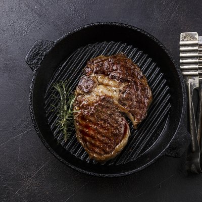 Grilled rib eye steak and tongs on grill pan on dark background
